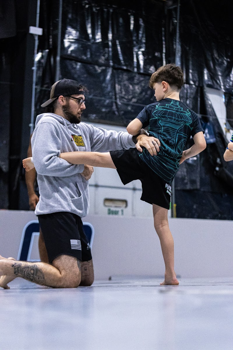 Coach kneeling to guide a young student through a high kick